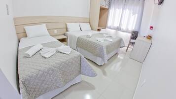 Une chambre d’hôtel avec deux lits, chacun recouvert d’une courtepointe matelassée et agrémenté d’oreillers blancs. On y trouve une tête de lit en bois, une petite table avec une chaise et une fenêtre avec des rideaux.