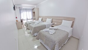 A hotel room with three beds, each with a white headboard and a quilted bedspread. There is a small table with a chair, a nightstand, and a TV mounted on the wall. - North Hotel (Chapecó)
