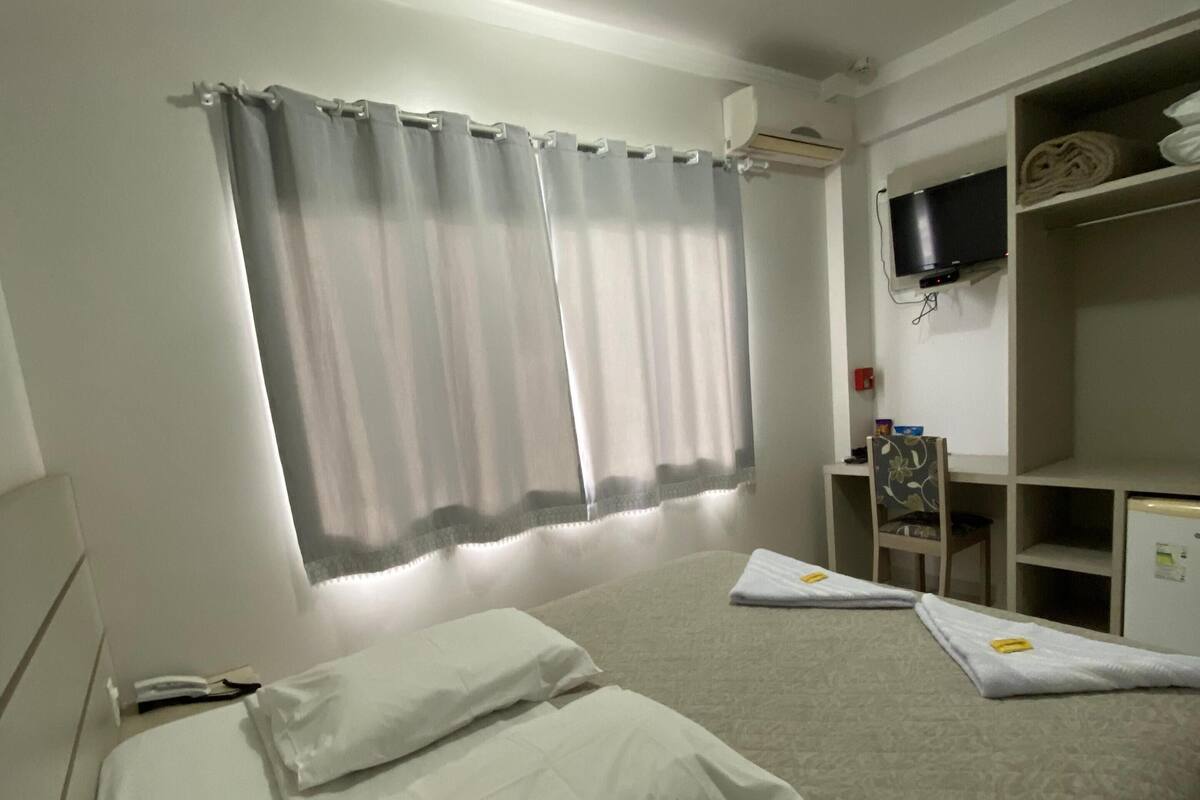 A hotel room with a bed, a TV mounted on the wall, and a shelf with items.