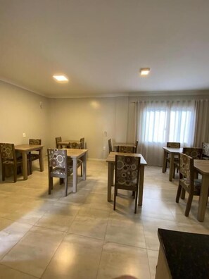 A dining area with multiple tables and chairs, a tiled floor, and a window with curtains. - North Hotel (Chapecó)