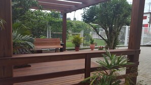 A wooden bench and potted plants in a covered outdoor area with a view of a fenced sports field. - North Hotel (Chapecó)