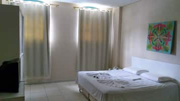 Una habitación de hotel con cama, cortinas, un cuadro y un teléfono sobre una mesita de noche.