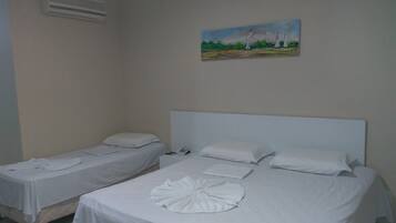 Deux lits simples avec du linge de lit blanc, un tableau représentant des arbres accroché au mur et un téléphone sur l’un des lits.