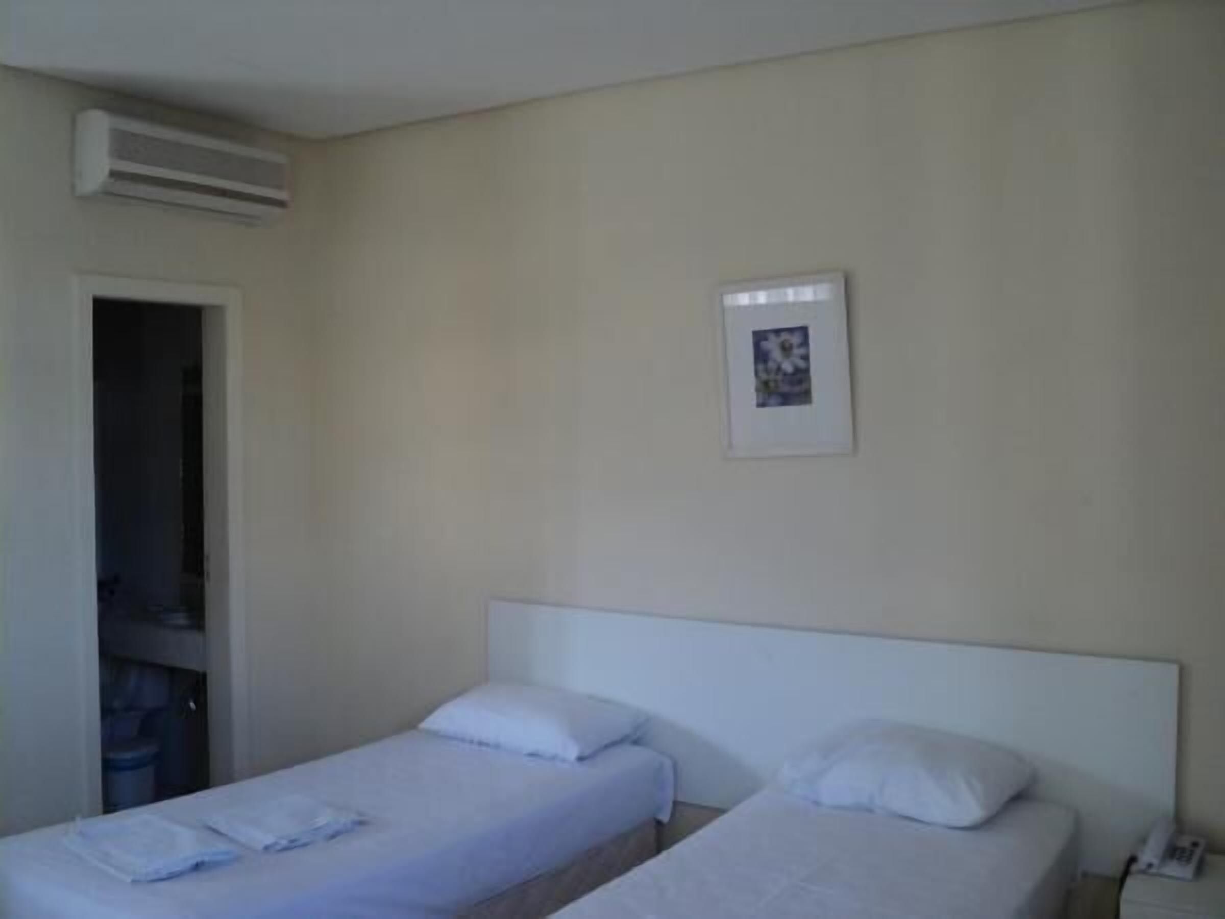 A hotel room with two single beds, a door leading to a bathroom, and a small framed picture on the wall.