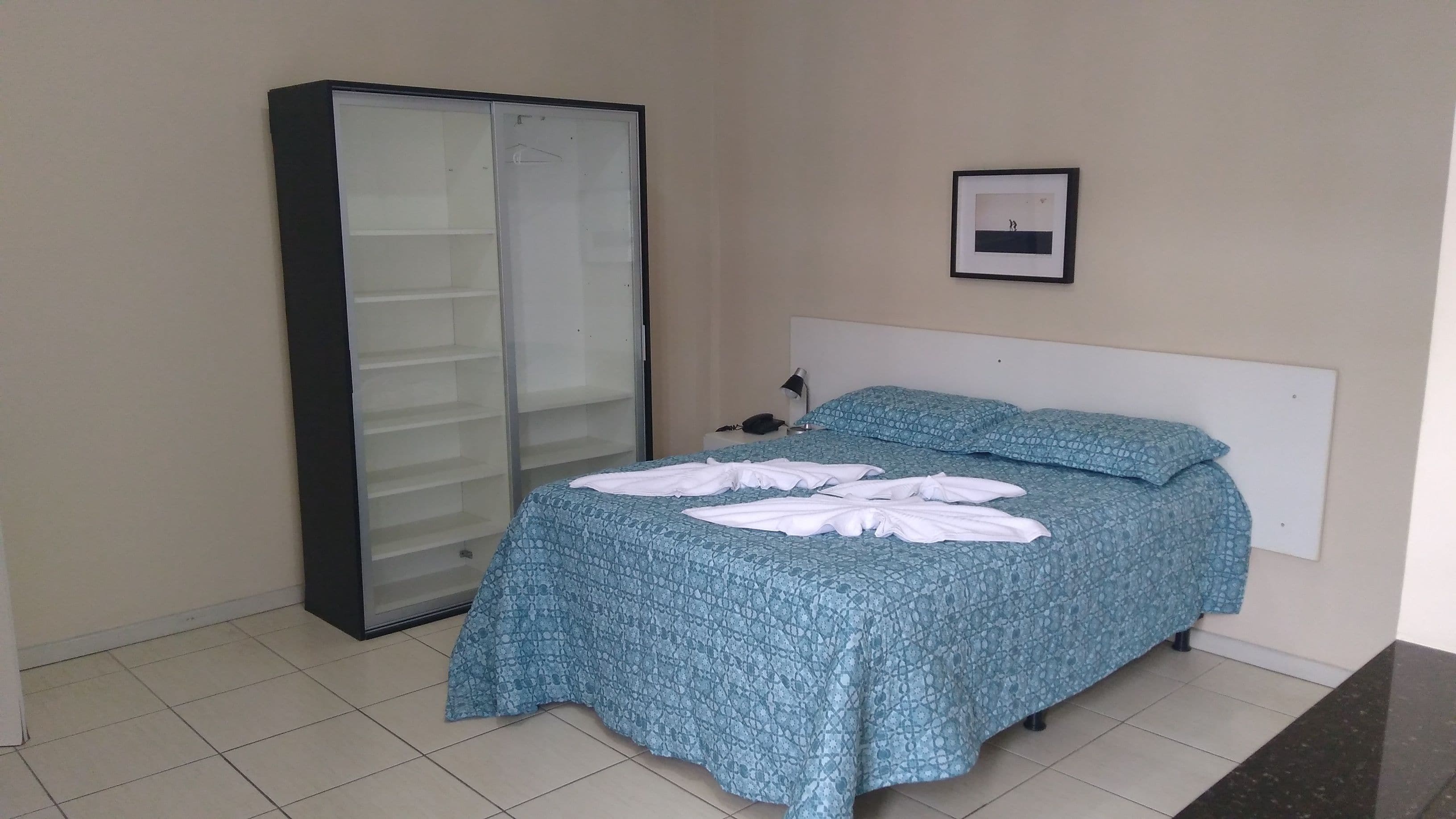 A bedroom with a bed, a wardrobe, a bedside lamp, and a framed picture on the wall.