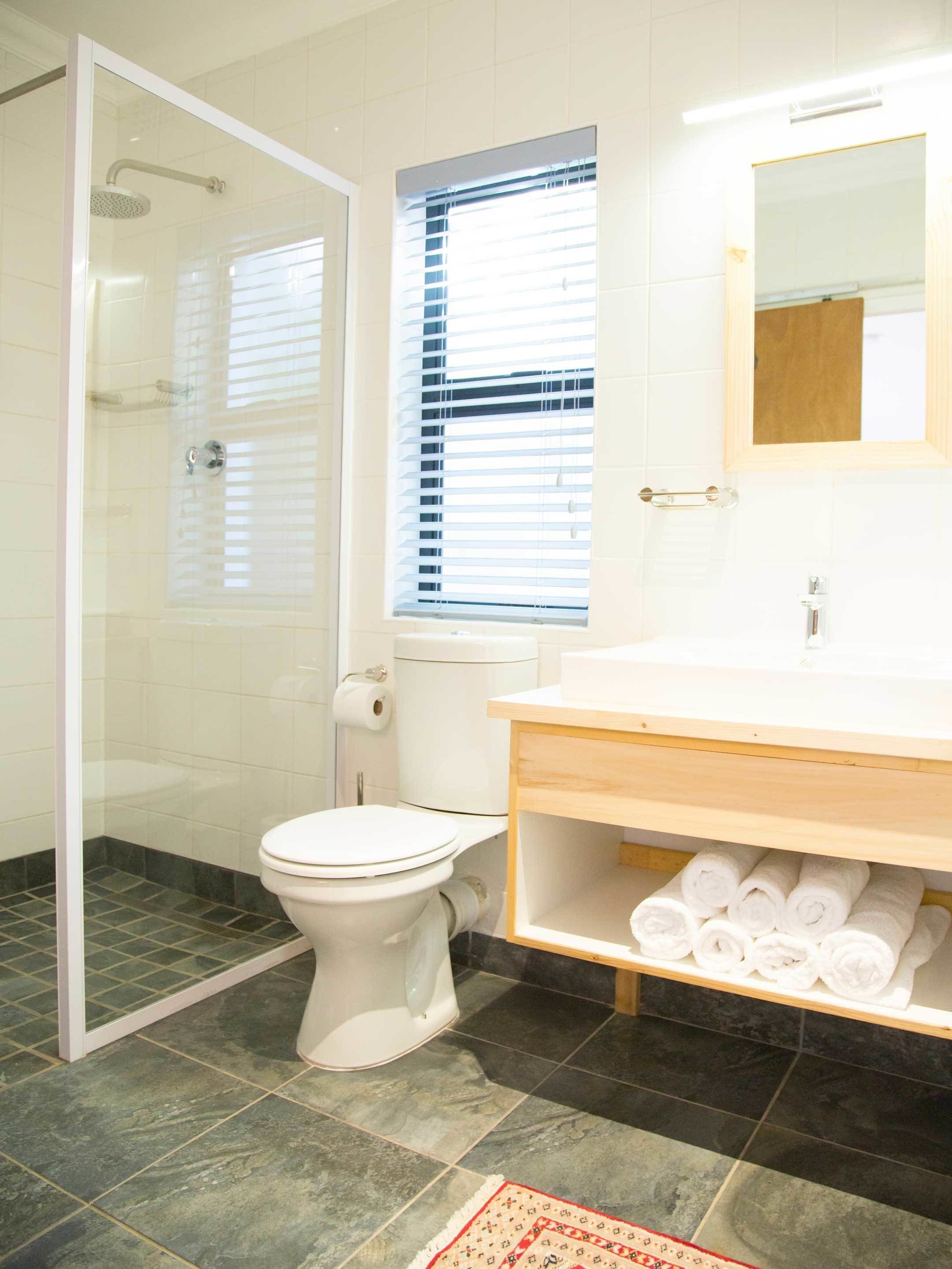 A bathroom with a glass shower enclosure, a toilet, a sink with a mirror, and a towel rack.