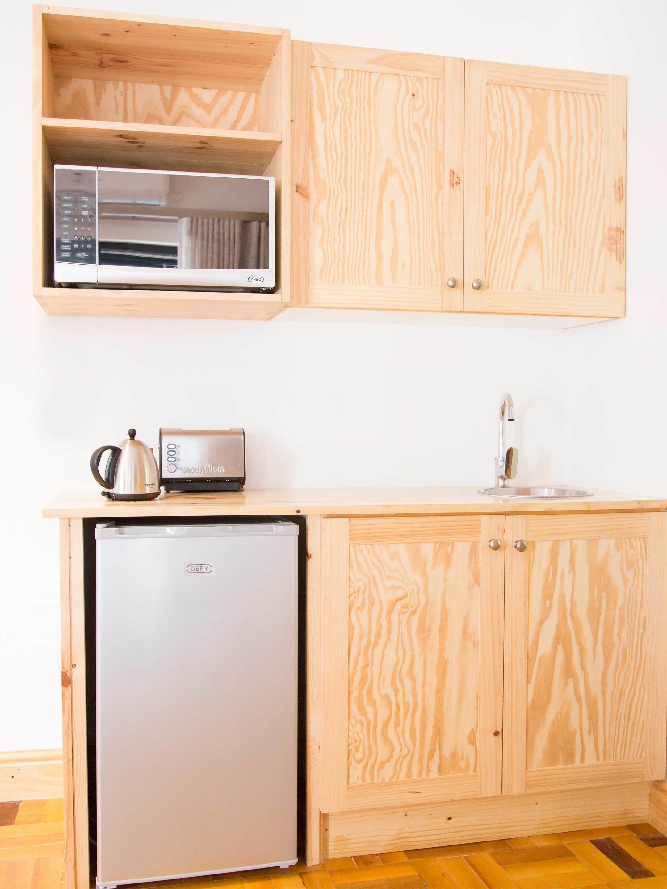 Una cocina compacta con armarios de madera, microondas integrado, tostadora y refrigerador pequeño.
