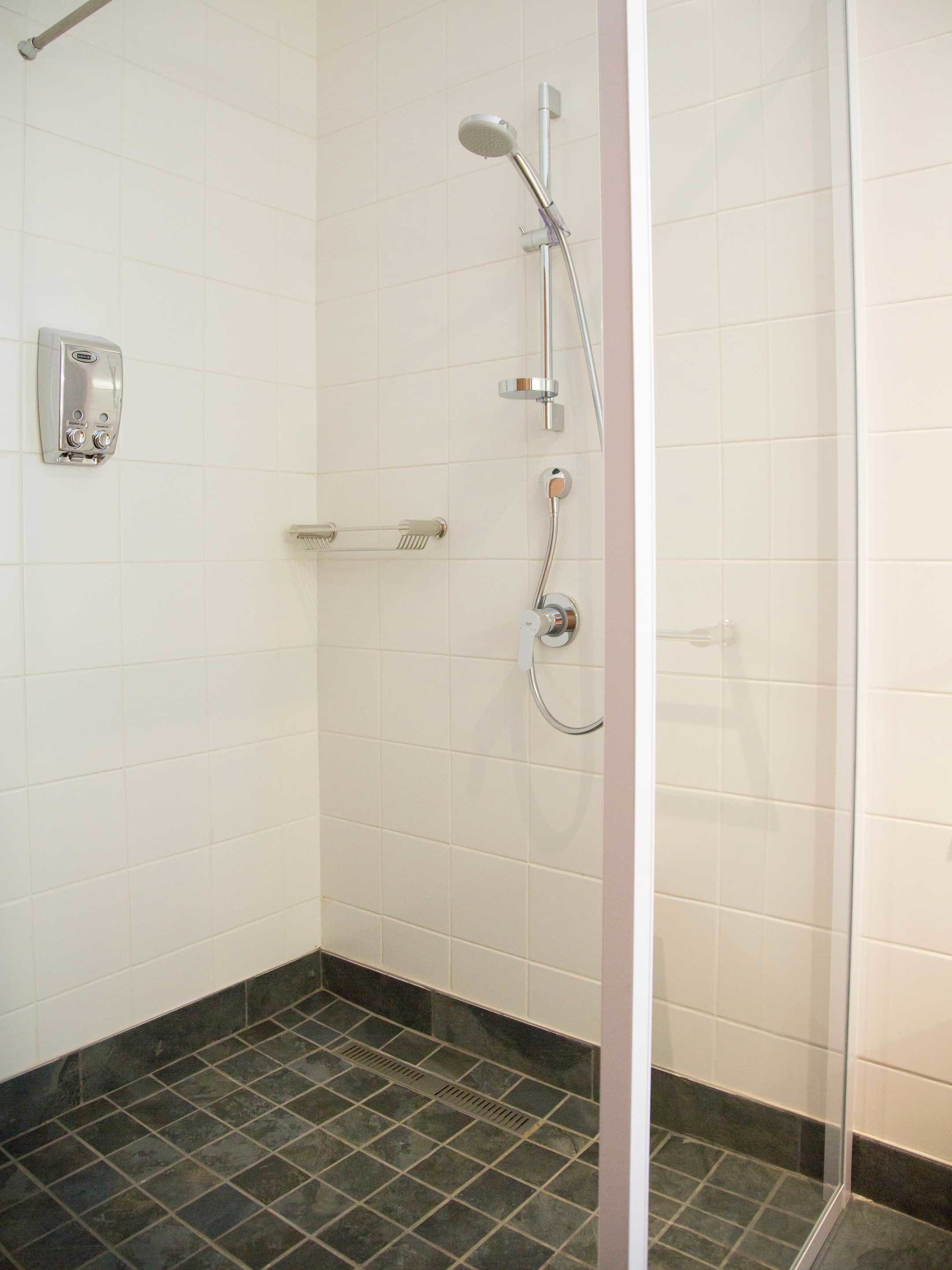 A shower with a handheld showerhead, a wall-mounted soap dispenser, and a towel rack.