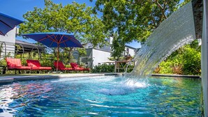 A swimming pool with a water feature, red lounge chairs, and a blue umbrella. - La Fontaine (Franschhoek)