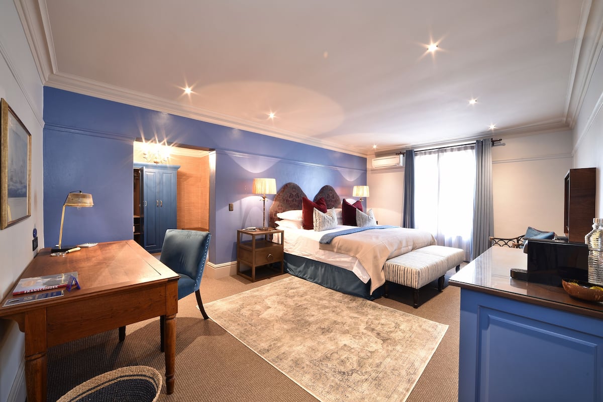 A hotel room with a bed, bedside tables, a desk, a chair, and a large window with curtains.