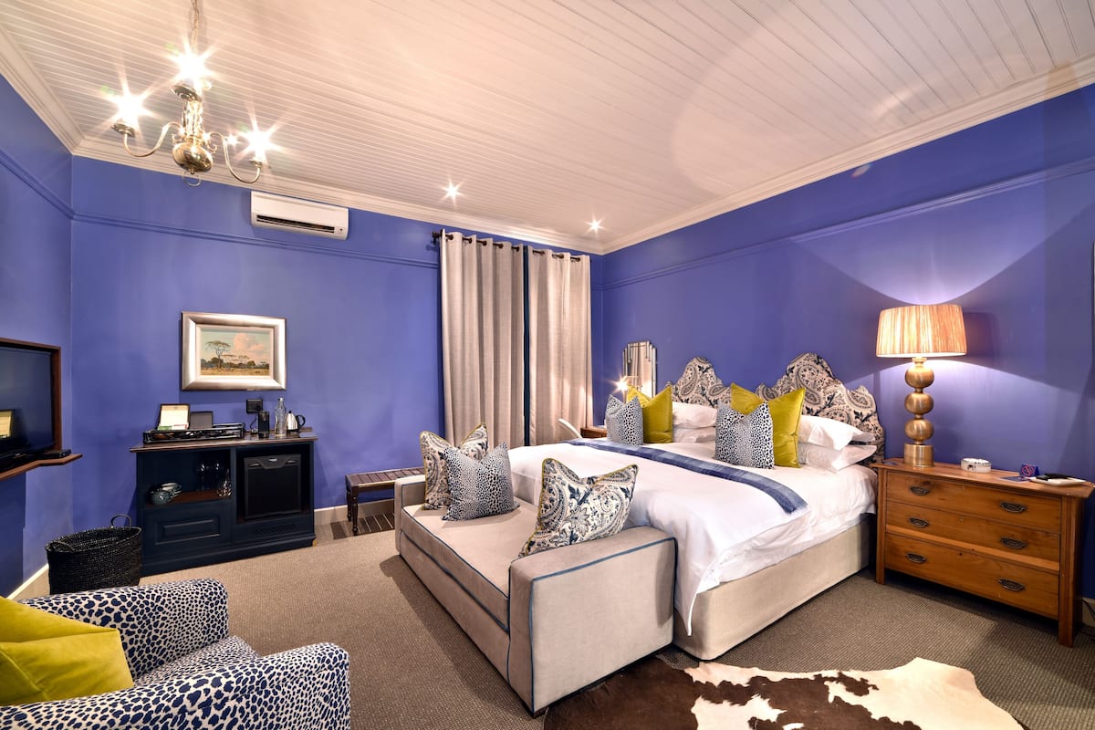 A bedroom with a large bed, a nightstand, a dresser, a sofa, and a chandelier.