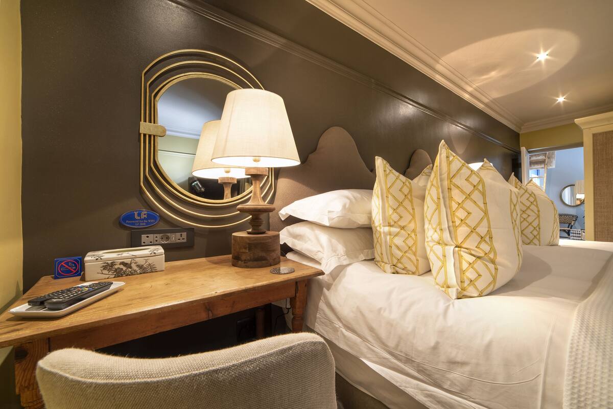 A hotel room with a bed, a bedside table with a lamp, a mirror, and a chair.