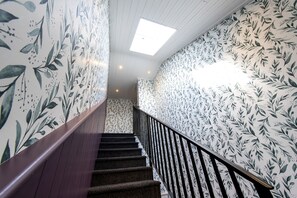 A staircase with a wooden handrail and black balusters, surrounded by wallpaper with a leafy pattern.