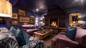 A cozy living room with a fireplace, purple sofas, and a coffee table. - La Fontaine (Franschhoek)