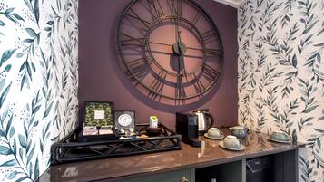 Una cocina con un gran reloj de pared, una cafetera y una bandeja con tazas y una tetera.