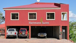 Een rood gebouw met het bord "Hartmann Suites" en drie geparkeerde voertuigen ervoor.