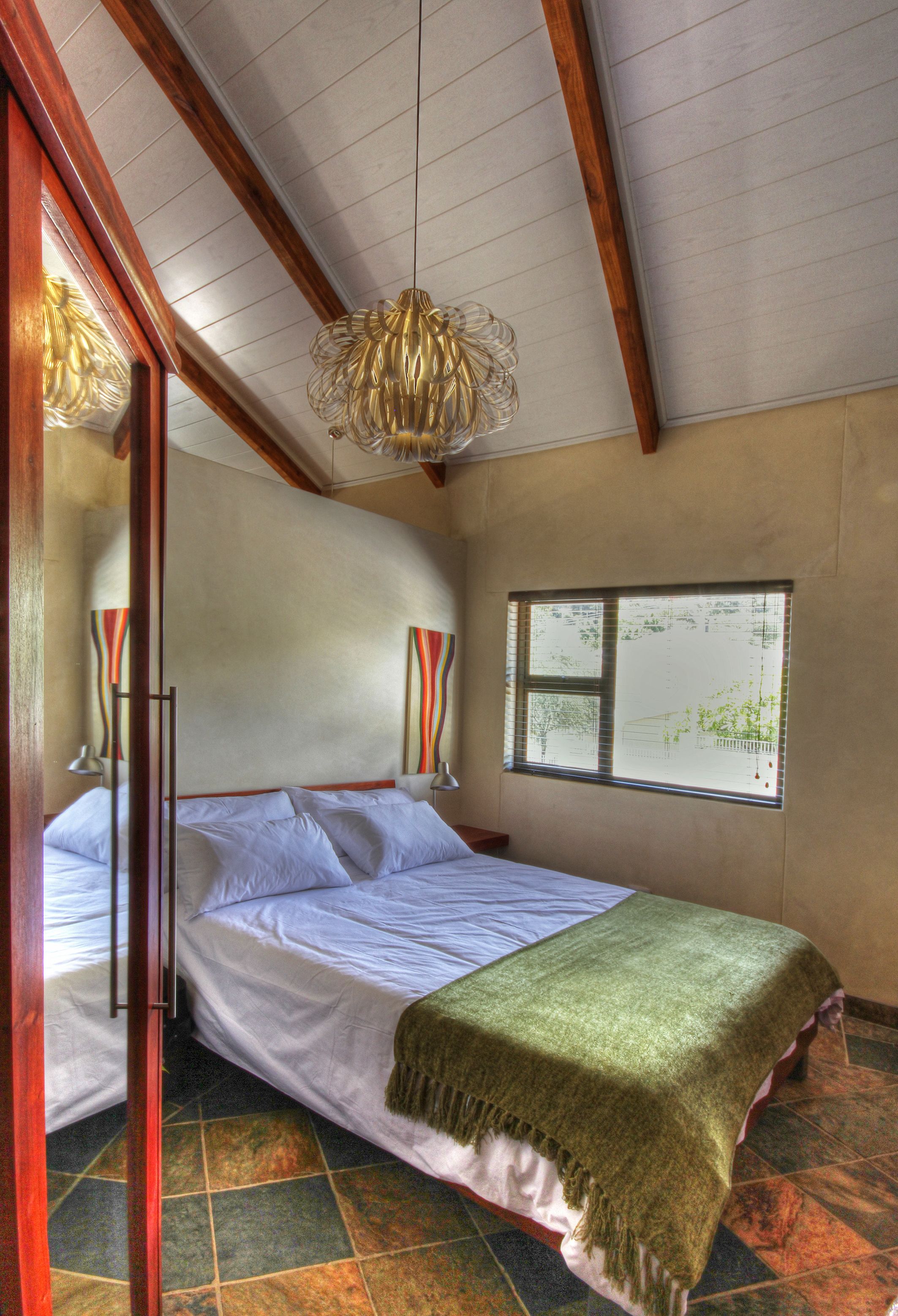 A bedroom with a bed, a window, and a hanging light fixture.