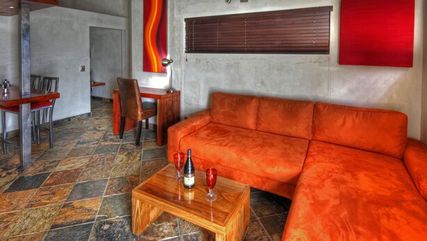 Een moderne woonkamer met een modulaire bank, een houten salontafel met een fles en glazen, en een eethoek met stoelen en een tafel.