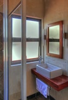 Een badkamer met een douchecabine van glas, een witte wastafel en een houten opbergmeubel.