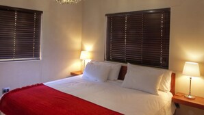 Een slaapkamer met een groot bed, houten balken, een kroonluchter, twee bedlampjes en een rode plaid.