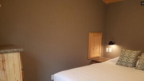 Ein Schlafzimmer mit einem großen Bett, einem Holzschrank, einem Nachttisch mit Lampe und gemusterten Kissen.