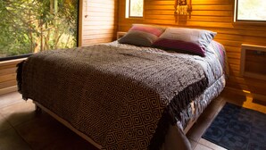 Ein Schlafzimmer mit Bett, Holzbalken, einem Fenster und einer Wandleuchte.