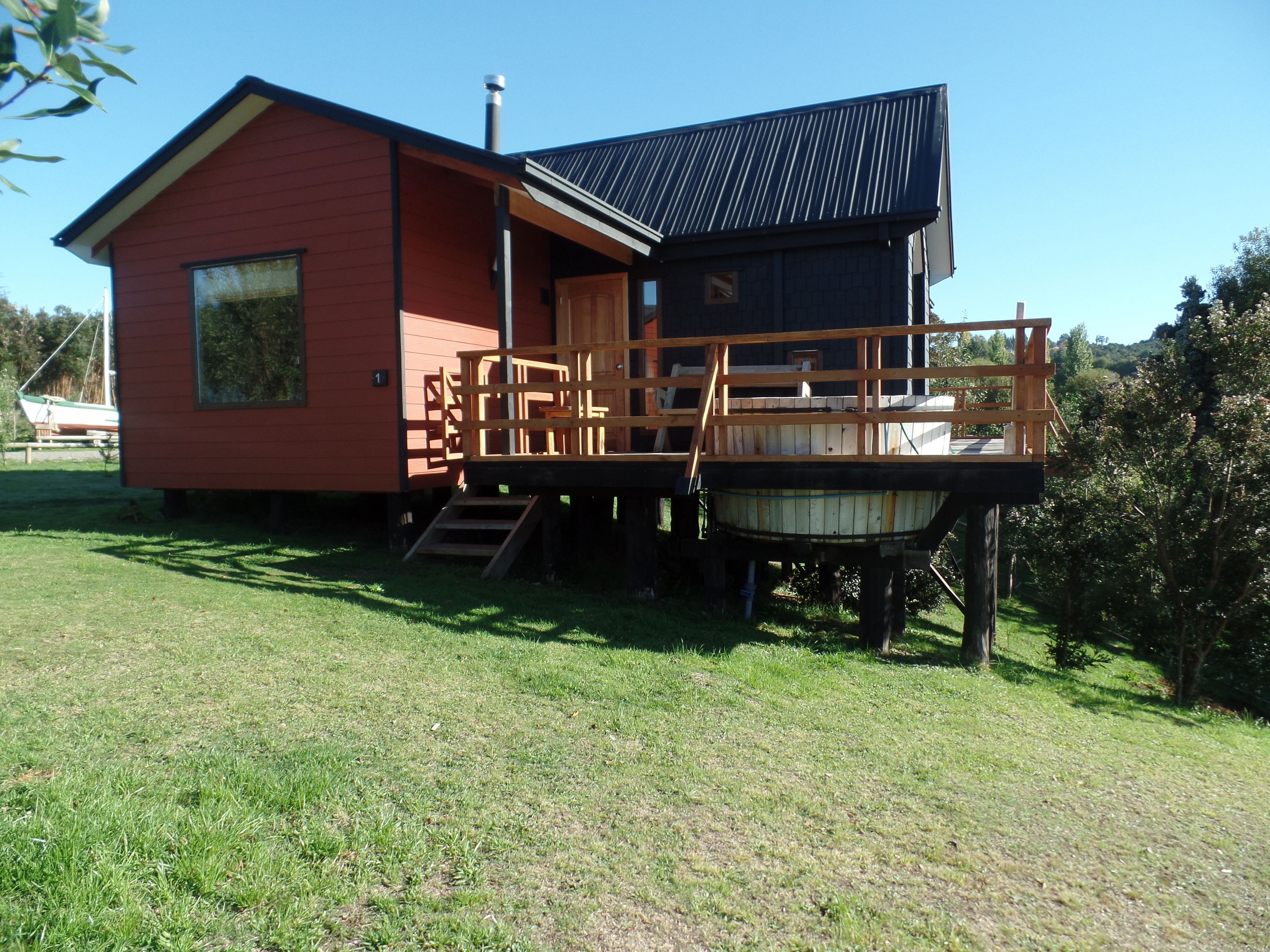 A red cabin with a wooden deck and a hot tub.