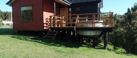 A red cabin with a wooden deck and a hot tub.