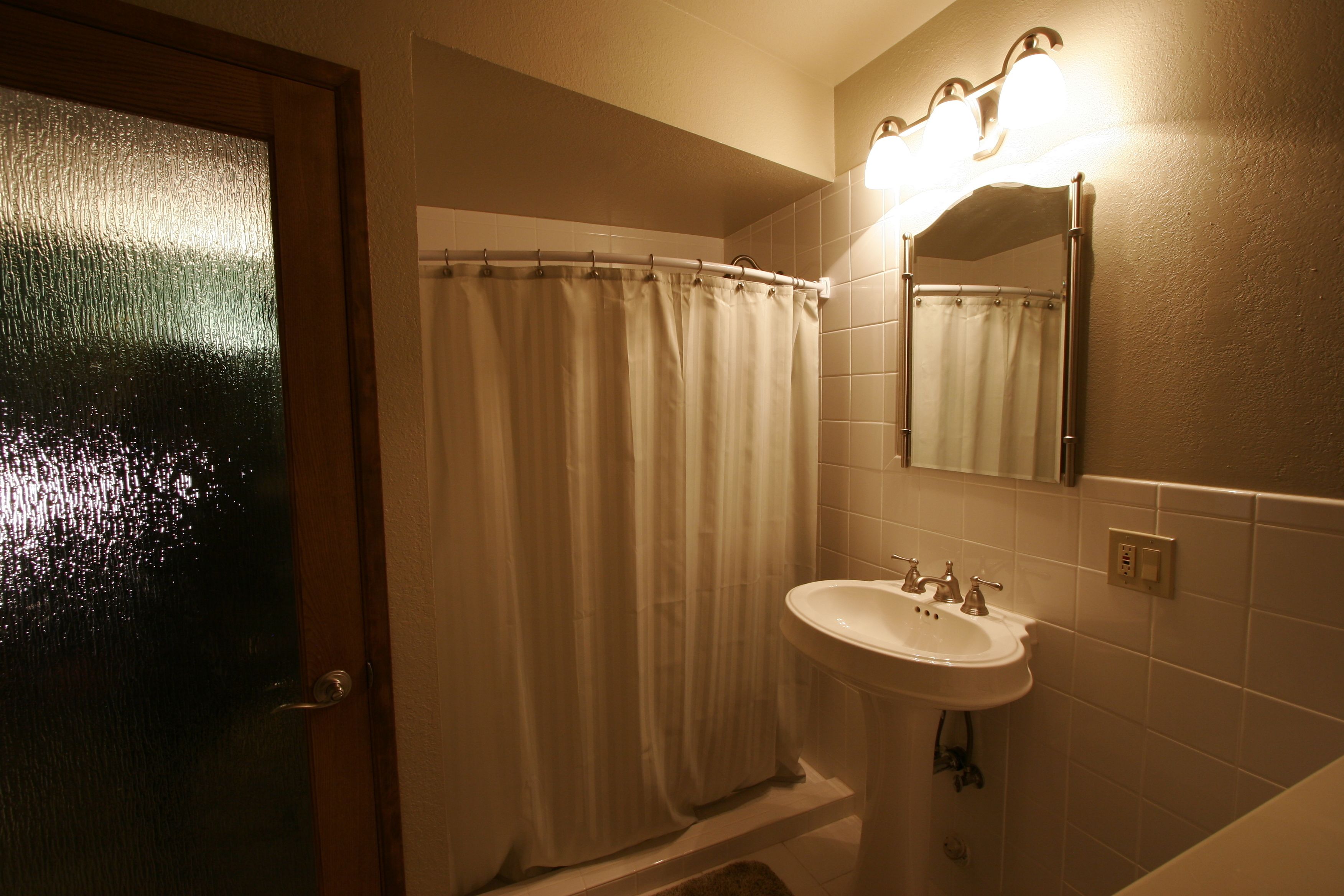 A bathroom with a shower curtain, a sink, and a mirror.