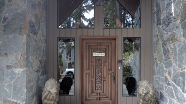 Une entrée en pierre, avec une porte en bois, deux statues de lions en pierre et un paillasson.