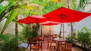 Un espace patio intérieur avec des tables et des chaises en bois, entouré d’une végétation luxuriante et agr émenté de parasols rouges.