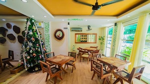 Un espace repas avec des tables et des chaises en bois, un sapin de Noël et un ventilateur de plafond.