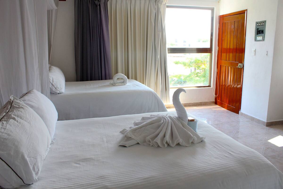 A hotel room with two beds, a window with curtains, and a wooden door.