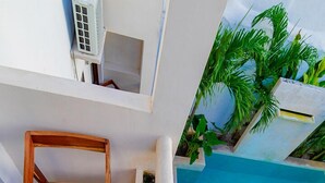 Une terrasse sur le toit avec une piscine, des meubles en bois et des plantes tropicales.