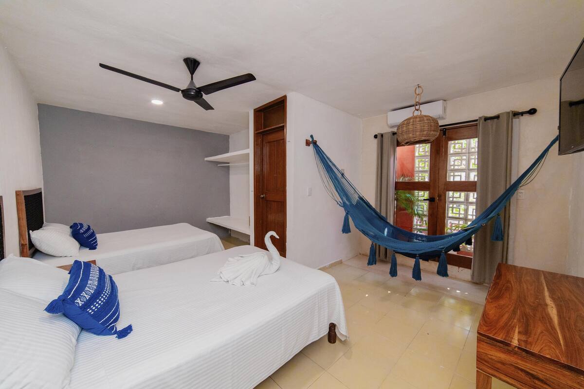 A hotel room with two beds, a ceiling fan, a hammock, and a TV.