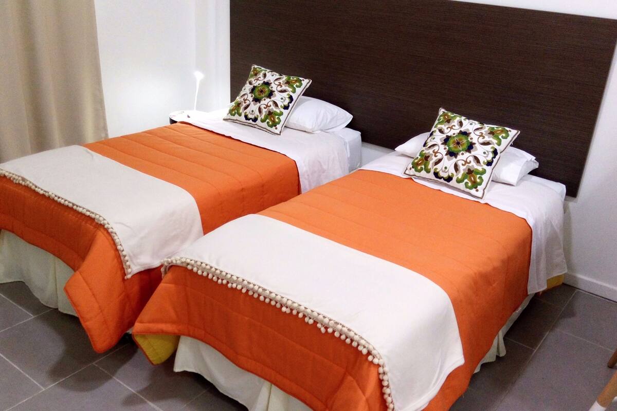 Two single beds with orange bedding and white pillows, a dark headboard, and a tiled floor.