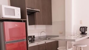 Une cuisine compacte équipée d’un four à micro-ondes, d’un réfrigérateur rouge, de meubles en bois, d’un évier et de deux tabourets de bar.