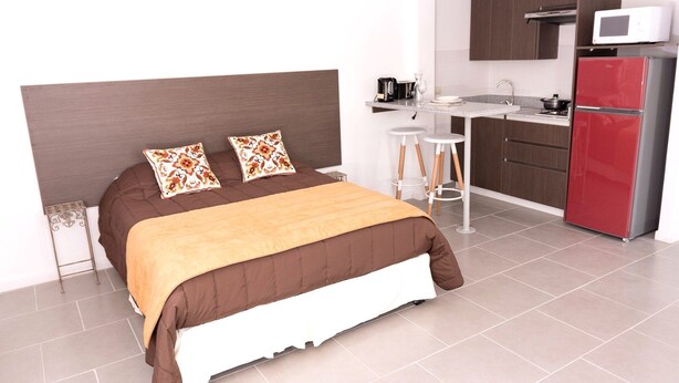 Une chambre d’hôtel moderne équipée d’un lit, d’une kitchenette et d’un réfrigérateur rouge.