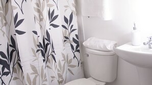 Une salle de bain équipée de toilettes, d’un lavabo et d’un rideau de douche orné d’un motif de feuilles.