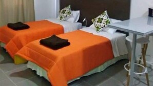 Une chambre d’hôtel avec deux lits simples, chacun recouvert d’une couverture orange et agrémenté d’oreillers blancs, une petite table et un rideau.