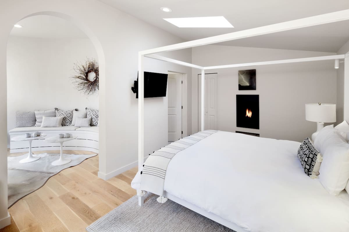 A modern bedroom with a white canopy bed, a flat-screen TV, and a fireplace.