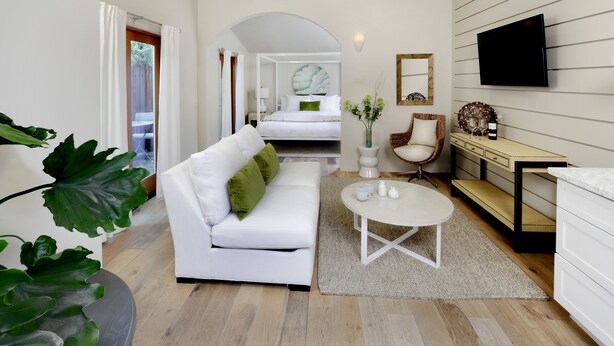 A modern hotel room with a white sofa, a round coffee table, a TV mounted on the wall, and a bed with a circular headboard. - Rockhouse Suites (Healdsburg)