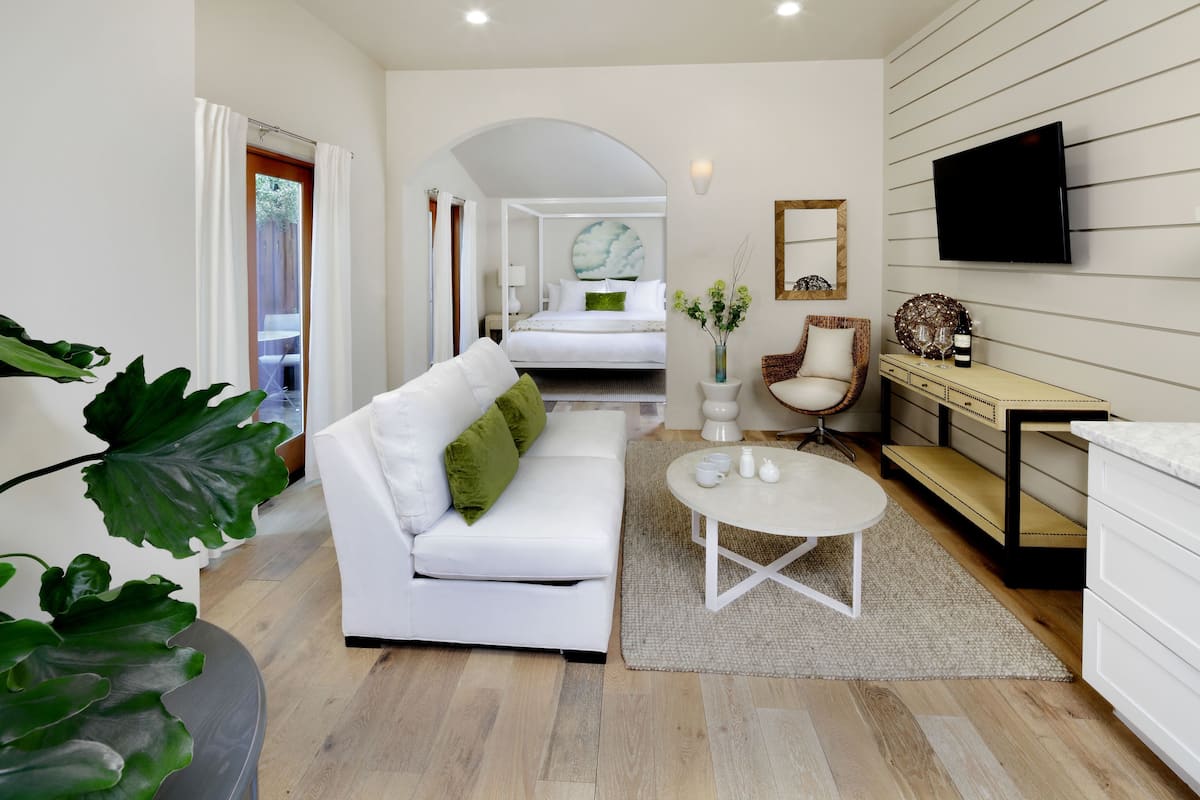 A modern hotel room with a white sofa, a round coffee table, a TV mounted on the wall, and a bed with a circular headboard.