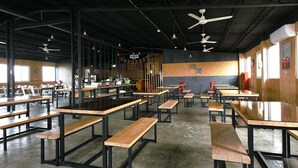 A spacious indoor dining area with multiple wooden tables and benches, ceiling fans, and a brick wall with a 'C' logo. - Good Night Hotel (Taoyuan City)