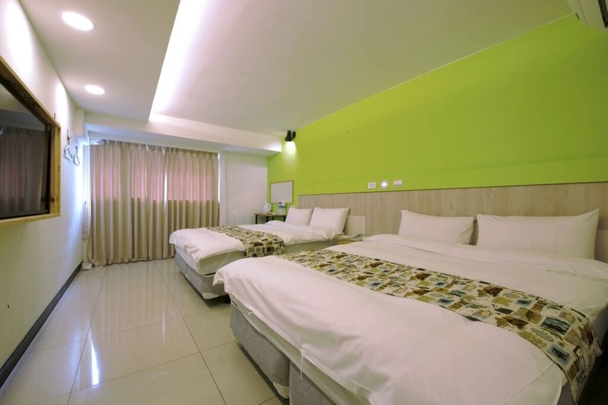 Une chambre d’hôtel avec deux lits, une grande fenêtre avec des rideaux, un miroir et un mur d’accent vert.