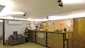 A reception area with a wooden reception desk, a brown sofa with blue cushions, a Christmas tree, and a wall clock. - Good Night Hotel (Taoyuan City)