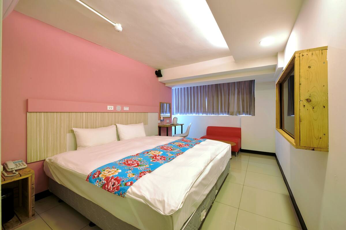 Une chambre d’hôtel comprenant un lit, un bureau avec un téléphone, une chaise, une fenêtre avec des rideaux et une armoire en bois.