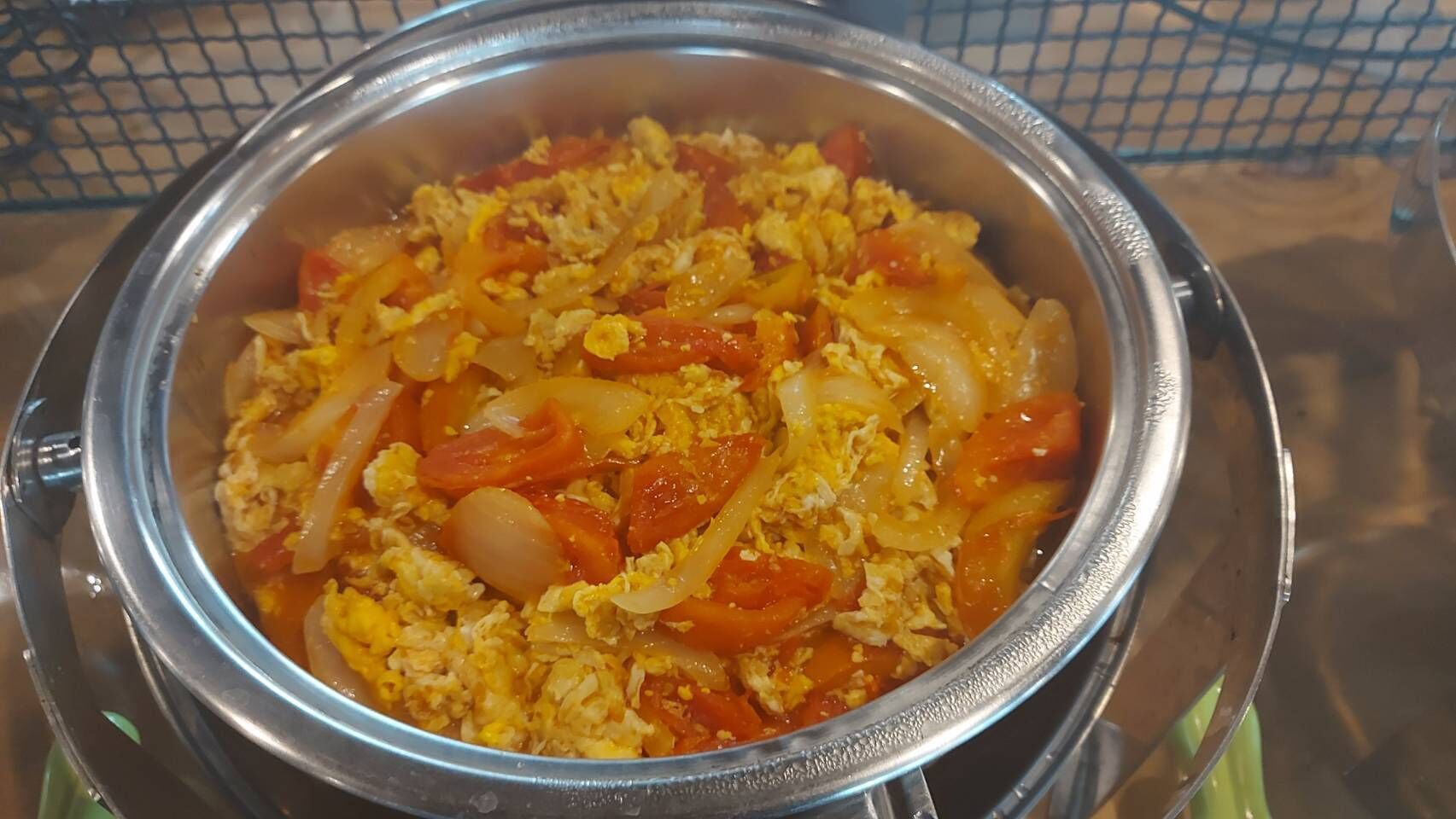 A stainless steel bowl containing scrambled eggs with tomatoes and onions.