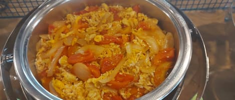A stainless steel bowl containing scrambled eggs with tomatoes and onions.