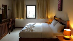 A hotel room with a bed, a desk, a chair, a window with curtains, a lamp, and a painting on the wall. - Same Same Guesthouse (Patong)